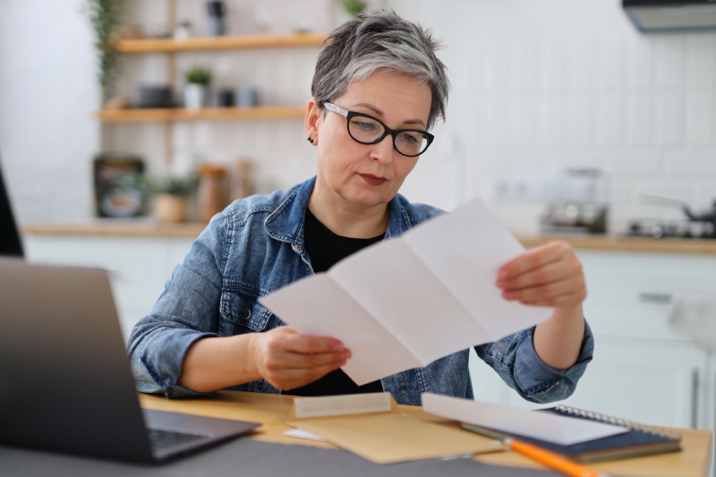 Older woman reading a letter from her mortgage company holding her insurance check